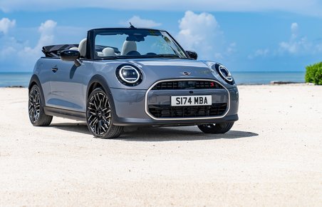 Blå-grå Mini Cabrio med kalechen nede på strand.