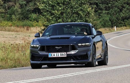En sort Ford Mustang set forfra, kørende gennem en naturskøn rute.
