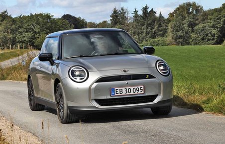 En sølvgrå Mini Cooper set forfra på en snoet, landlig vej.