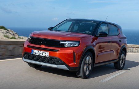 Rød Opel Frontera kører i sving på bjergvej med havet i baggrunden