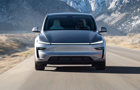 En grå faceliftet Tesla Model Y kører på vej med bjerge i baggrunden. 