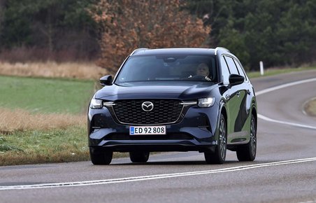 Mazda CX-80 set forfra kører i et sving på en landevej