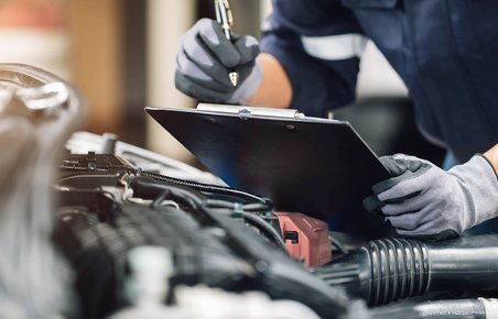 Mekaniker tager noter under serviceeftersyn. Motor kan ses i forgrunden. 