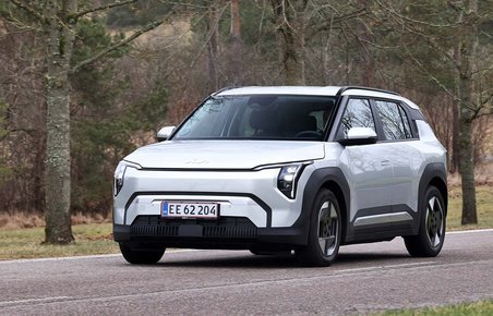Kia EV3 set skråt forfra, mens den kører på vej mellem træer