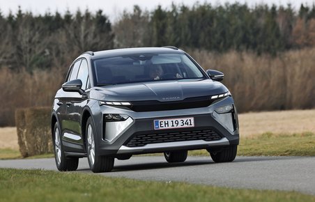 Skoda Elroq 50 set forfra, mens den kører på en landevej med træer og marker i baggrunden