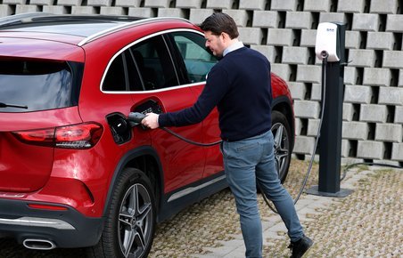 Mand sætter ladestik i rød plugin-hybrid.