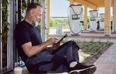 Mand sidder med kaffe og pc og venter på, at elbilen bliver ladet op