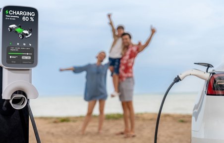Familie står på strand, mens elbil lades op i forgrunden