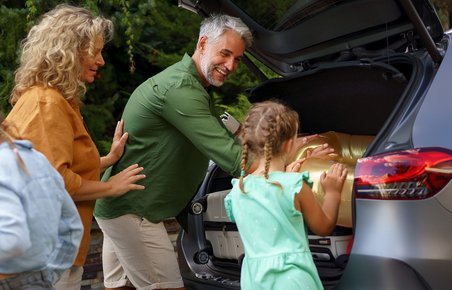 Familie med far, mor og to børn pakker bilen på vej på bilferie. 