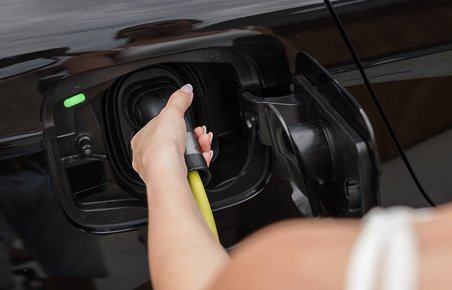 Kvinde sætter stik til opladning på en sort elbil